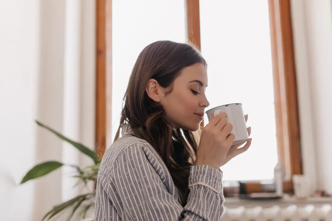 young-woman-striped-shirt-drinks-coffee-from-iron-cup-against-window[1]